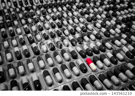 Red and white capsule among black and white capsules in overlapping blister packs, with individual compartments and silver foil backing, pharmaceutical packaging for oral medicine and pharmacy supply. Red and white capsule among black and white capsules in overlapping blister packs, with individual compartments and silver foil backing, pharmaceutical packaging for oral medicine and pharmacy supply. 143561210