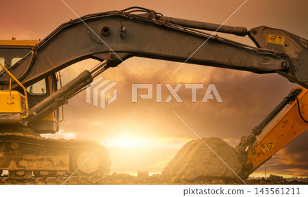 Backhoe parked at construction site after digging soil. Bulldozer on sunset sky and clouds background. Digger after work. Earth moving machine at construction site at dusk. Digger with dirt bucket. Backhoe parked at construction site after digging soil. Bulldozer on sunset sky and clouds background. Digger after work. Earth moving machine at construction site at dusk. Digger with dirt bucket. 143561211
