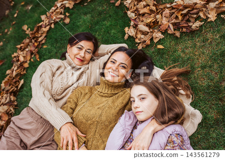 Mother, grandmother and daughter, laying on grass in the middle of heart from leaves. Mother, grandmother and daughter, laying on grass in the middle of heart from leaves. 143561279