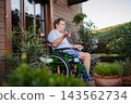 Senior man in wheelchair exercising with resistance band on terrace. 143562734