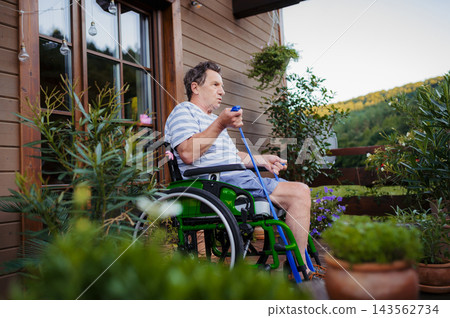 Senior man in wheelchair exercising with resistance band on terrace. Senior man in wheelchair exercising with resistance band on terrace. 143562734