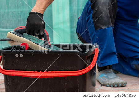 Construction worker cleaning a grout float in a bucket Construction worker cleaning a grout float in a bucket 143564850