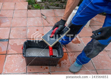 Worker applying grout on tiled floor with hand tools outdoors Worker applying grout on tiled floor with hand tools outdoors 143564851