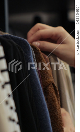 Vertical video. Woman choosing clothes from rack with hangers inside room. Lady looks to clothes, decides what to wear. Lifestyle women relax at home. Vertical video. Woman choosing clothes from rack with hangers inside room. Lady looks to clothes, decides what to wear. Lifestyle women relax at home. 143564994