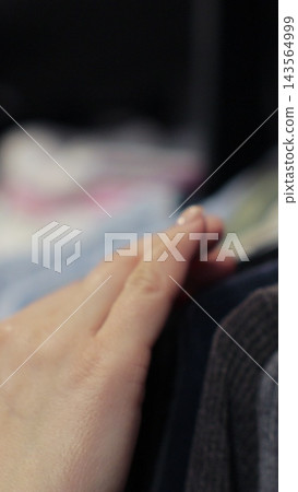 Vertical video. Woman hand runs across a rack of clothes at house or store. Home wardrobe or clothing shop changing room. Vertical video. Woman hand runs across a rack of clothes at house or store. Home wardrobe or clothing shop changing room. 143564999