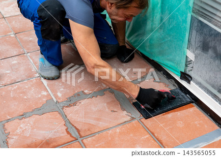 Worker installing floor tiles with trowel during renovation project 143565055