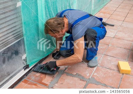 Worker grouting outdoor terracotta tiles beside covered glass storefront Worker grouting outdoor terracotta tiles beside covered glass storefront 143565056