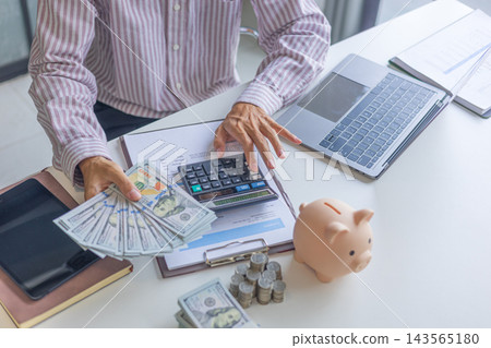 Businessman counting cash and organizing finances with money and piggy bank on the table. Businessman counting cash and organizing finances with money and piggy bank on the table. 143565180