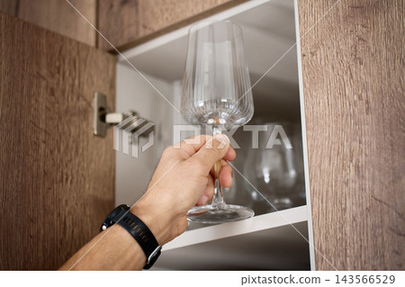 Person taking a wine glass from a kitchen cabinet Person taking a wine glass from a kitchen cabinet 143566529