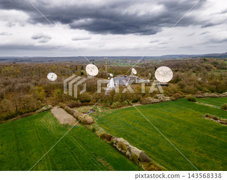 Aerial satellite ground station with parabolic dish array. Aerial drone view of satellite ground station with multiple large parabolic dish antennas pointed skyward amid green countryside, telecommuni Aerial satellite ground station with parabolic dish array. Aerial drone view of satellite ground station with multiple large parabolic dish antennas pointed skyward amid green countryside, telecommuni 143568338