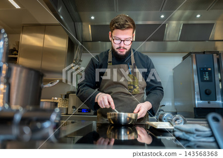 Restaurant Chef Preparing a Dish. Handsome chef in uniform cooking and preparing a dish in a restaurant kitchen. 143568368