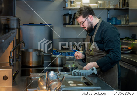 Chef Preparing Food in Culinary Workspace. Handsome male chef cooking fresh ingredients in a professional culinary workspace. Chef Preparing Food in Culinary Workspace. Handsome male chef cooking fresh ingredients in a professional culinary workspace. 143568369