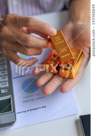 Physical gold bars on investor's hand at office desk. Concept for secure financial investment and wealth preservation. Physical gold bars on investor's hand at office desk. Concept for secure financial investment and wealth preservation. 143568849