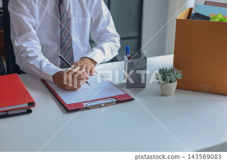 Employee signing exit paperwork next to box of personal belongings. Employee signing exit paperwork next to box of personal belongings. 143569083
