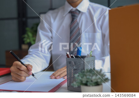 Employee signing exit paperwork next to box of personal belongings. Employee signing exit paperwork next to box of personal belongings. 143569084