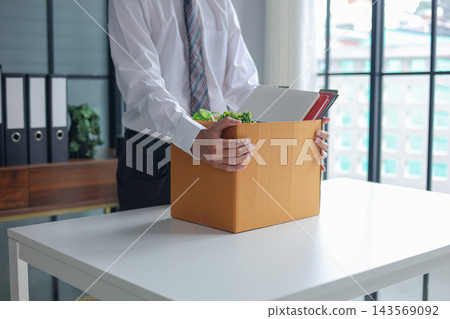 Businessman holding cardboard box with office supplies after resigning from job. Businessman holding cardboard box with office supplies after resigning from job. 143569092