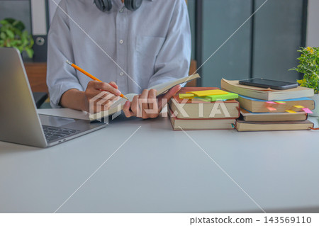 College Student Writing Research Notes During Online Learning and Academic Study Session at Home. 143569110