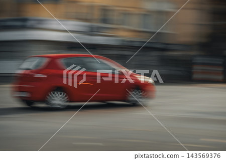 Red Car Driving on City Road, Motion Blur. Red passenger car travels along urban roadway with blurred buildings, passing traffic. Blurred vehicle speed, city transportation, dynamic street movement Red Car Driving on City Road, Motion Blur. Red passenger car travels along urban roadway with blurred buildings, passing traffic. Blurred vehicle speed, city transportation, dynamic street movement 143569376