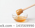 Honey dripping from a honey dipper into a glass dish against a white background. 143569990