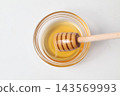 Honey in a glass container and a honey dipper, viewed from directly above. 143569993