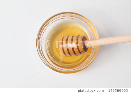 Honey in a glass container and a honey dipper, viewed from directly above. 143569993