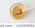Honey in a glass container and a honey dipper, viewed from directly above. 143569994