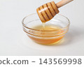Honey dripping from a honey dipper into a glass dish against a white background. 143569998
