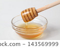 Honey dripping from a honey dipper into a glass dish against a white background. 143569999