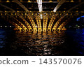 The underside structure of Kuramae Bridge on the Sumida River, its golden arch ribs, and the reflection of light on the dark water surface. 143570076