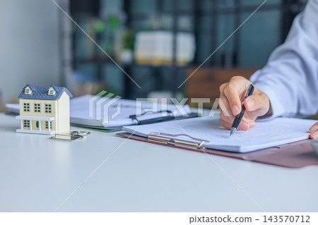 Businessman reading contract document next to miniature house on the table in office. Concept for real estate investment, loan, rent, mortgage, insurance Businessman reading contract document next to miniature house on the table in office. Concept for real estate investment, loan, rent, mortgage, insurance 143570712