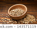 Roasted sunflower seed kernels in a bowl and scattered close-up on a wooden background. 143571119