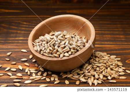 Roasted sunflower seed kernels in a bowl and scattered close-up on a wooden background. 143571119