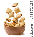 Cereal pads falling in a wooden bowl on a white background. Isolated 143571124