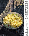 Pasta is cooked in a pot over an open fire in a natural setting. The scene shows a campfire and the surrounding outdoors, conveying a moment of 143572326