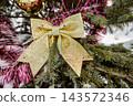 A Christmas and New Year tree stands in the snow with gold decorations and a large gold bow. The setting is winter with snow covering the ground 143572346