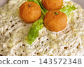 A plate holds a dish topped with small orange balls and green lettuce. The dessert is made with a creamy base and is presented nicely 143572348