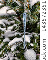 A Christmas tree stands adorned with decorations and surrounded by snow. Ornaments hang from the branches while the ground is covered in white 143572351