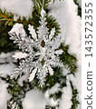 A decorated tree stands covered in snow during winter. The tree has ornaments that highlight the festive season 143572355