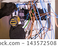 Electrician using an electric screwdriver to install wiring in a breaker panel box. 143572508