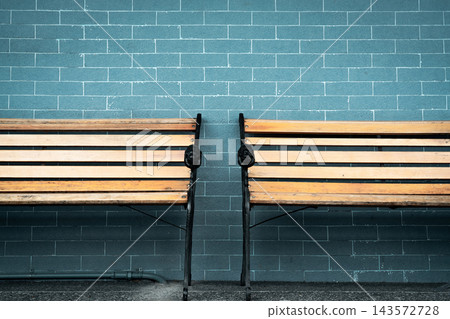 Two empty wooden benches with brown slatted seats and black metal frames beside a green tiled wall outside a building, decorative lion heads on the armrests and weathered surfaces in a waiting area. 143572728