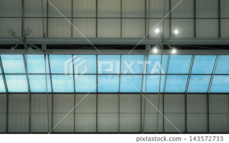 Airport roof with glass skylights and ceiling mounted LED lamps, rectangular panes framed by metal supports beside panels, modern interior architecture combining glazing and energy saving lighting. Airport roof with glass skylights and ceiling mounted LED lamps, rectangular panes framed by metal supports beside panels, modern interior architecture combining glazing and energy saving lighting. 143572733