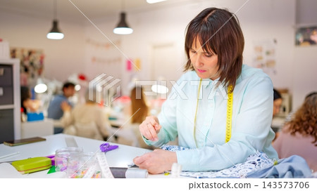 Seamstress hand stitching lace fabric in a sewing workshop Seamstress hand stitching lace fabric in a sewing workshop 143573706