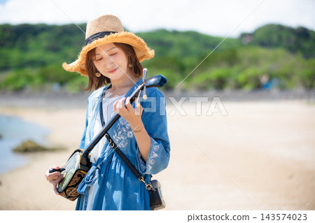 一位女模特兒在沖繩海灘上彈奏三弦琴。 一位女模特兒在沖繩海灘上彈奏三弦琴。 143574023