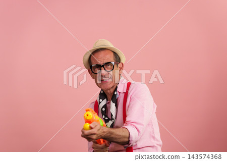Senior man having fun with water gun on pink background Senior man having fun with water gun on pink background 143574368