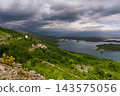 Stormy Sky Over Green Hills and Island-Dotted Lake With Small Rural Houses and Dramatic Clouds 143575056