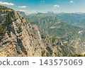 Dramatic Mountain Cliff Overlooking Expansive Green Canyon Landscape Under Clear Blue Sky 143575069
