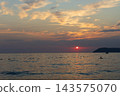 Sunset Over Calm Sea With Silhouetted Swimmer and Boat Near Distant Island 143575070