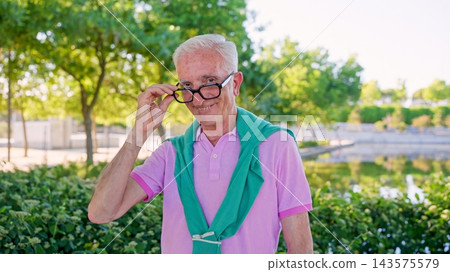 Smiling senior man holding glasses in park Smiling senior man holding glasses in park 143575579