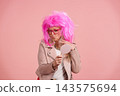 Mature woman wearing pink wig checking appearance in mirror 143575694