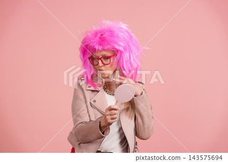 Mature woman wearing pink wig checking appearance in mirror 143575694